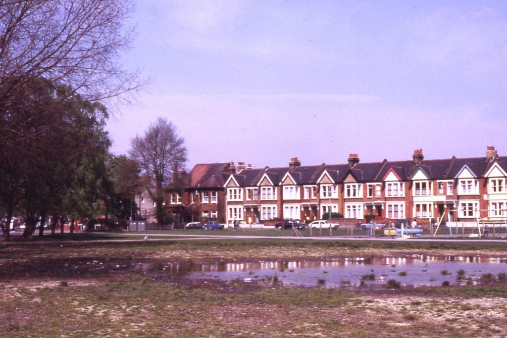 Figges Marsh with Gorringe Park Avenue in background, Mitcham, Surrey CR4. Pond forming on site of old air-raid shelter and earlier pond. Little Graveney ran along eastern (right-hand) side of Marsh