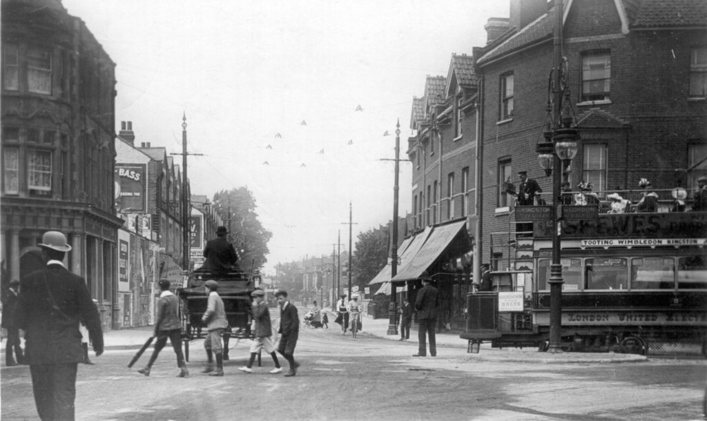Postmarked 1907, the year in which Wimbledon saw its first trams, this view looks up Merton Road. A LUT tram is swinging round from Merton High Street. It advertises Skewes store in Wimbledon, as well as Sandown Park Races.